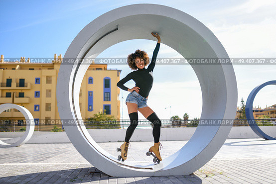 Young fit black woman on roller skates riding outdoors on urban street. Smiling girl with afro hairstyle rollerblading on sunny day. Стоковое фото, агентство Ingram Publishing / Фотобанк Лори