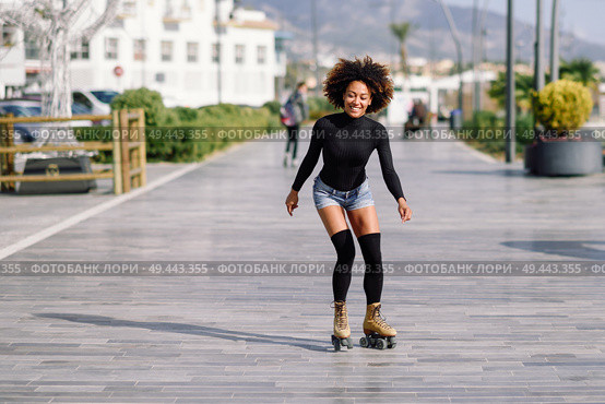 Young fit black woman on roller skates riding outdoors on urban street. Smiling girl with afro hairstyle rollerblading on sunny day. Black woman on roller skates riding outdoors on urban street. Стоковое фото, агентство Ingram Publishing / Фотобанк Лори
