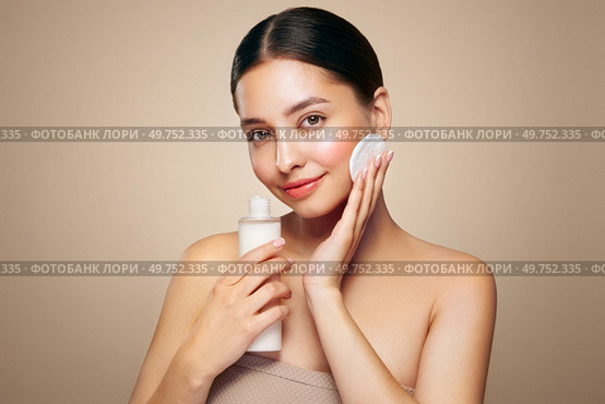 Young girl holds cotton pad while cleansing face with cosmetic milk. Skin care removal of makeup cleansing. Basic facial skin care. Стоковое фото, агентство Ingram Publishing / Фотобанк Лори