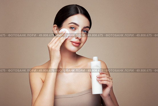 Young girl holds cotton pad while cleansing face with cosmetic milk. Skin care removal of makeup cleansing. Basic facial skin care. Стоковое фото, агентство Ingram Publishing / Фотобанк Лори