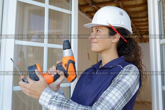 young happy woman in uniforl makes renovations with drill. Стоковое фото, агентство Ingram Publishing / Фотобанк Лори