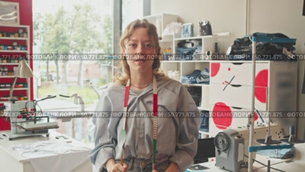 young, lovely dressmaker, standing in her workshop. She is surrounded by sewing tools and has measuring tape around her neck. Стоковое видео, видеограф Strunov David / Фотобанк Лори