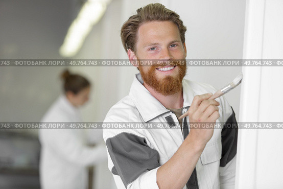 young male worker holding paint brush next to the wall. Стоковое фото, агентство Ingram Publishing / Фотобанк Лори