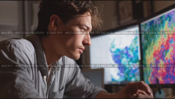 Young man analyzes colorful data on multiple screens in a dimly lit workspace in the evening. Стоковое AI-видео, аниматор Сергей Толмачёв / Фотобанк Лори