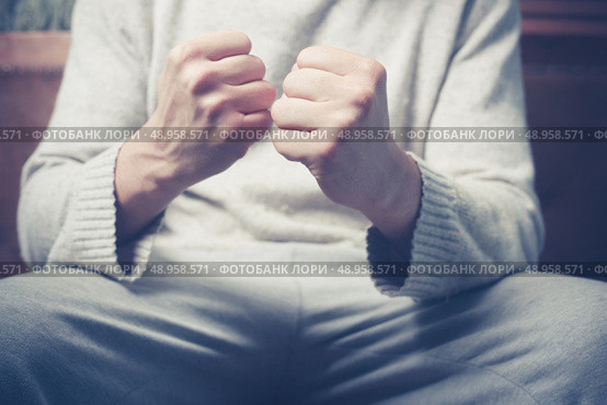Young man is sitting on a sofa with his fists clenched. Стоковое фото, агентство Ingram Publishing / Фотобанк Лори