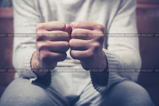 Young man is sitting on a sofa with his fists clenched. Стоковое фото, агентство Ingram Publishing / Фотобанк Лори