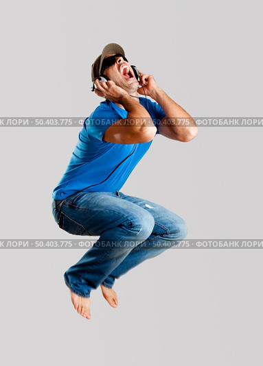 Young man jumping and listening music isolated over a gray background. Стоковое фото, агентство Ingram Publishing / Фотобанк Лори