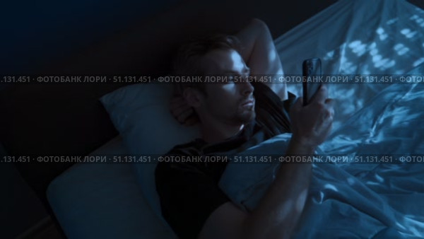 Young man uses his phone at night in bed, scrolling through his social media. Стоковое видео, видеограф Arsenii Palivoda / Фотобанк Лори