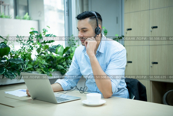 Young man working at a call center which is a consultant for various information of customers who call to inquire or ask for advice with a happy mood. Стоковое фото, агентство Ingram Publishing / Фотобанк Лори