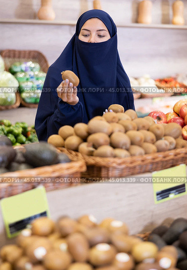 Young Muslim woman in niqab choosing ripe kiwi in market. Стоковое фото, фотограф Яков Филимонов / Фотобанк Лори