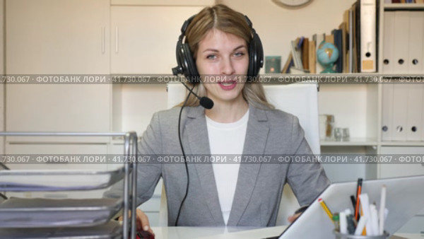 Young positive woman customer support phone operator in microphone headset working on laptop in the office. Стоковое видео, видеограф Яков Филимонов / Фотобанк Лори