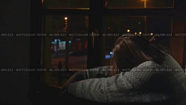 Young woman sits on window and looks sadly at night city. Стоковое фото, фотограф David Kashakhi / Фотобанк Лори