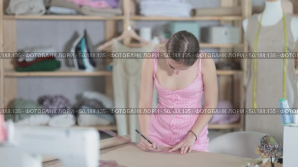 Young woman tailor drawing with pencil on brown paper, she sketching clothes and patterns on table in sewing workshop. Стоковое видео, видеограф Яков Филимонов / Фотобанк Лори