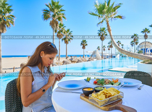 Young woman texting with smartphone chat on a swimming pool restaurant. Стоковое фото, агентство Ingram Publishing / Фотобанк Лори