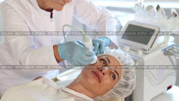 Young woman undergoing hardware facial treatment using high frequency ultrasound attachment stimulating opening of skin pores for deep penetration of moisturizers and nutrients at cosmetic clinic. Стоковое видео, видеограф Яков Филимонов / Фотобанк Лори
