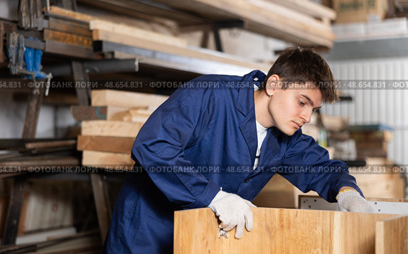 Young worker assembles a wooden table in furniture factory. Work process. Стоковое фото, фотограф Яков Филимонов / Фотобанк Лори