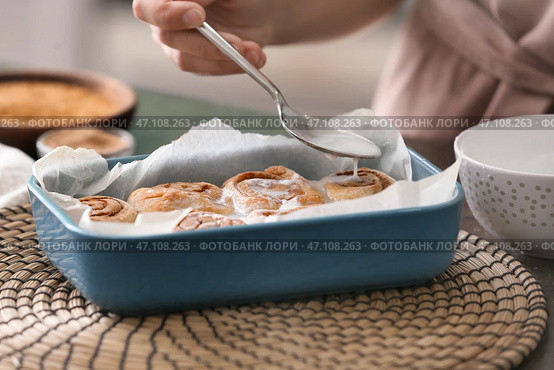 Женщина наливает сливки на вкусные булочки с корицей на столе. Стоковое фото, фотограф Pixel_shot / Фотобанк Лори