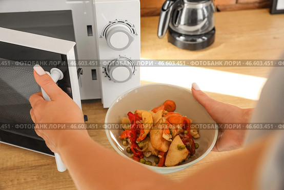 Женщина ставит миску с вкусной едой в современную микроволновую печь на деревянном столе. Стоковое фото, фотограф Pixel_shot / Фотобанк Лори