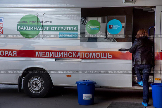 Женщина ждет своей очерди на вакцинацию у мобильного пункта бесплатной вакцинации от гриппа в специальном автомобиле скорой помощи в городе Москве, Россия (2023 год). Редакционное фото, фотограф Николай Винокуров / Фотобанк Лори