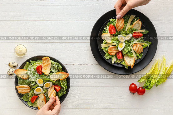 Женщины едят с вкусным салатом Цезарь на светлом деревянном фоне. Стоковое фото, фотограф Pixel_shot / Фотобанк Лори